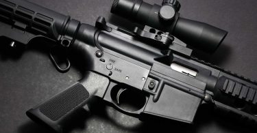 Close-up of an AR-15 receiver area showing the upper and lower receiver, trigger, magazine well, and optic mounted on the rail