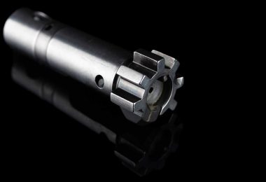 Close-up of an AR-15 bolt showing locking lugs and front face against a black background