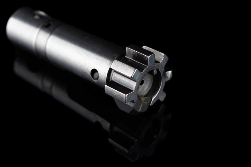 Close-up of an AR-15 bolt showing locking lugs and front face against a black background