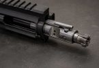 Bolt carrier group partially extended from an AR-15 upper receiver showing bolt lugs and cam pin on a workbench