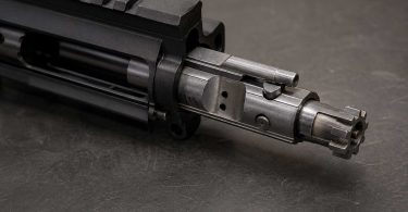 Bolt carrier group partially extended from an AR-15 upper receiver showing bolt lugs and cam pin on a workbench