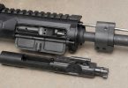 Close-up of an AR-15 upper receiver on a workbench with the gas block, gas tube, and partially removed bolt carrier group visible.