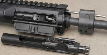 Close-up of an AR-15 upper receiver on a workbench with the gas block, gas tube, and partially removed bolt carrier group visible.