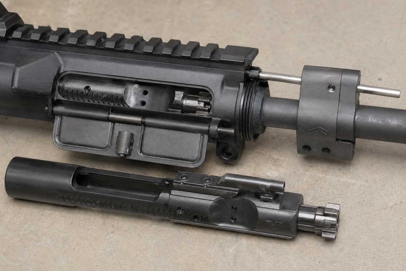 Close-up of an AR-15 upper receiver on a workbench with the gas block, gas tube, and partially removed bolt carrier group visible.