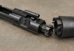 AR-15 bolt carrier group with bolt extended next to a barrel extension on a workbench