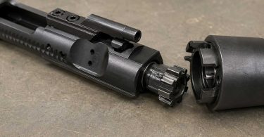 AR-15 bolt carrier group with bolt extended next to a barrel extension on a workbench