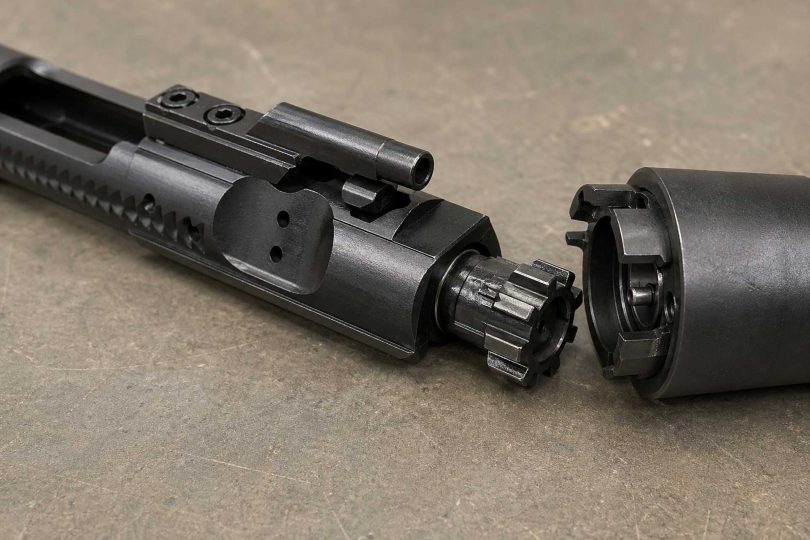 AR-15 bolt carrier group with bolt extended next to a barrel extension on a workbench