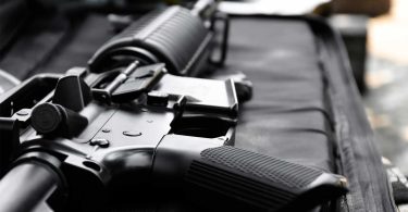 Close-up of a black AR-style rifle receiver and magazine resting on a padded surface