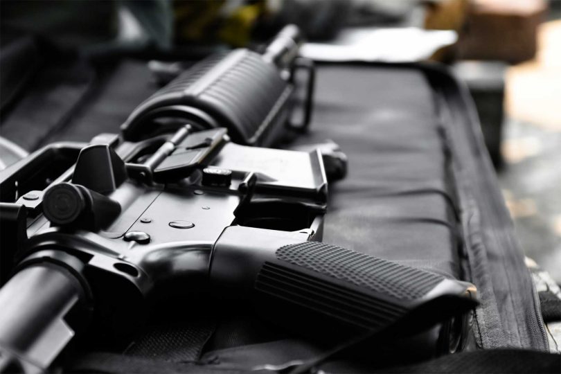Close-up of a black AR-style rifle receiver and magazine resting on a padded surface