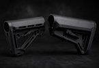 Two black AR-15 buttstocks placed facing each other on a dark textured surface with soft studio lighting