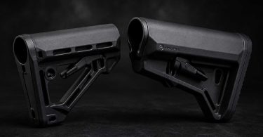 Two black AR-15 buttstocks placed facing each other on a dark textured surface with soft studio lighting