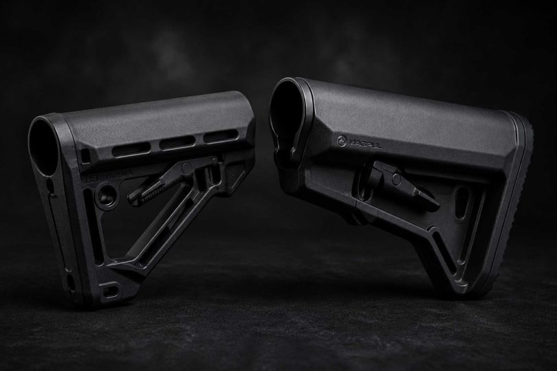 Two black AR-15 buttstocks placed facing each other on a dark textured surface with soft studio lighting
