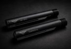 Two black AR-style buffer tubes labeled mil-spec and commercial placed side by side on a dark surface