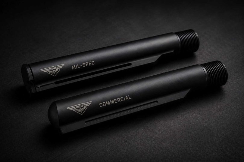 Two black AR-style buffer tubes labeled mil-spec and commercial placed side by side on a dark surface
