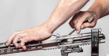 person cleaning the interior of an AR-style rifle upper receiver with a brush