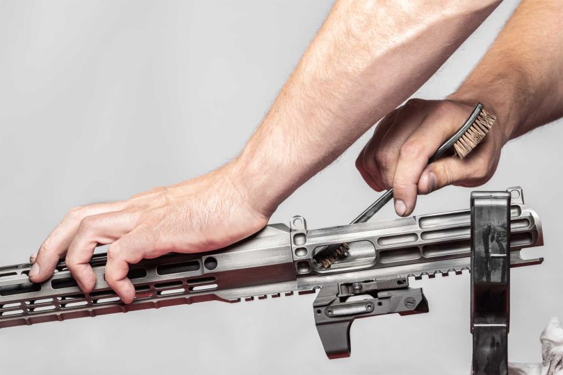 person cleaning the interior of an AR-style rifle upper receiver with a brush