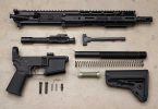 Disassembled AR-15 components arranged on a workbench, including upper receiver, lower receiver, bolt carrier group, and buffer system