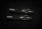 Two metallic bolt carrier groups placed parallel on a dark textured surface with soft directional lighting