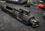 Close-up of a metal bolt carrier group resting on a dark workbench with tools blurred in the background