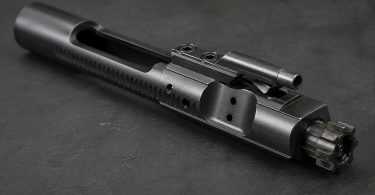 AR-15 bolt carrier group on a dark workbench showing bolt lugs and carrier body