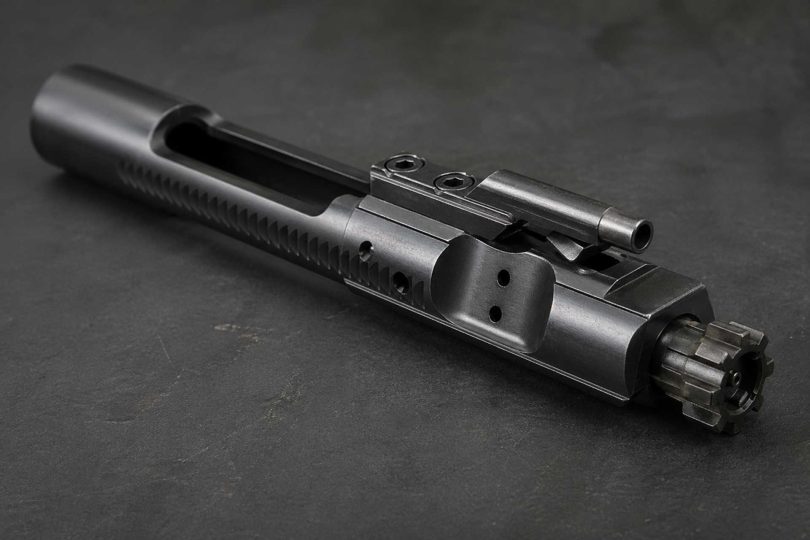 AR-15 bolt carrier group on a dark workbench showing bolt lugs and carrier body