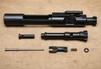 Disassembled bolt carrier group components arranged on a wooden surface, including the carrier, bolt, firing pin, cam pin, and small parts