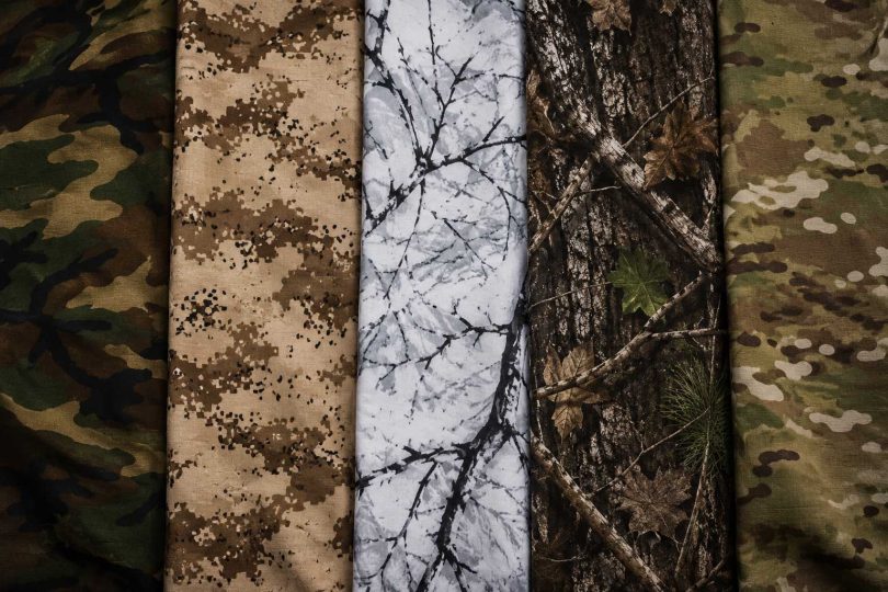Five camouflage fabric patterns displayed side by side, including woodland, desert, snow, tree bark, and multicam designs.