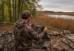 Hunter comparing several camouflage jackets beside a marsh and woodland landscape